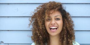 Cosmetic Dentistry - woman laughing blue background after having cosmetic dentistry treatment